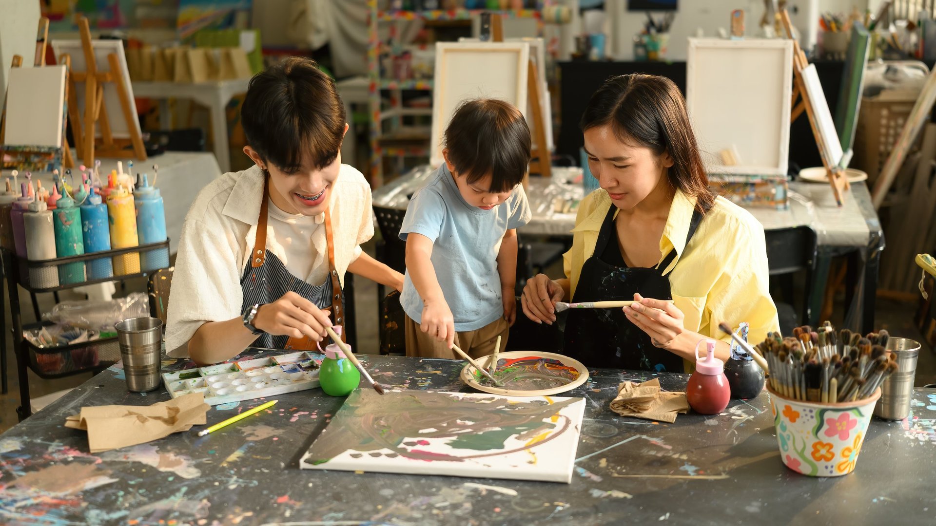 A preschool teacher assists a mother and child during an art class in a calm, stylish studio