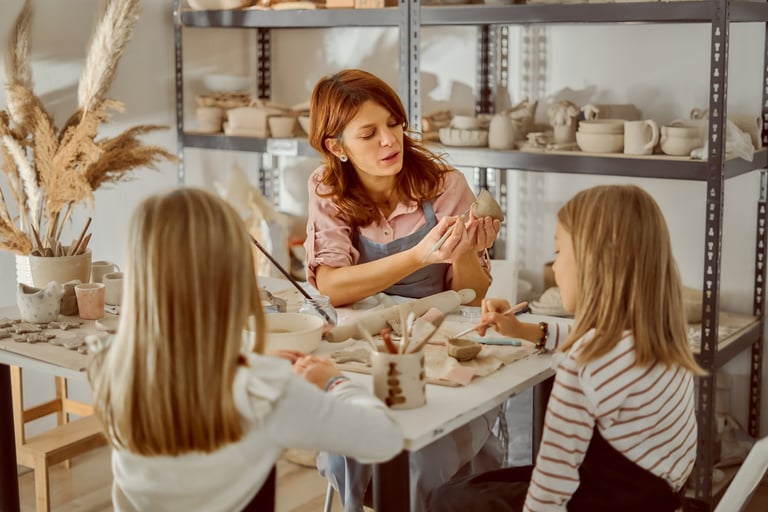Children during a hands-on creative session in a bright, organized studio with shelves filled with art pieces