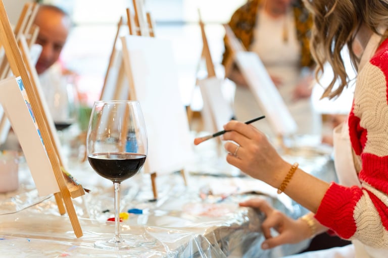 Woman painting on canvas while holding a paintbrush at a fun art and wine workshop for creative adults