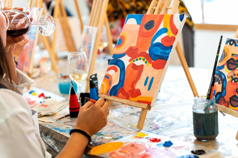 Woman holding a glass of red wine, painting an abstract canvas on an easel during a creative art workshop