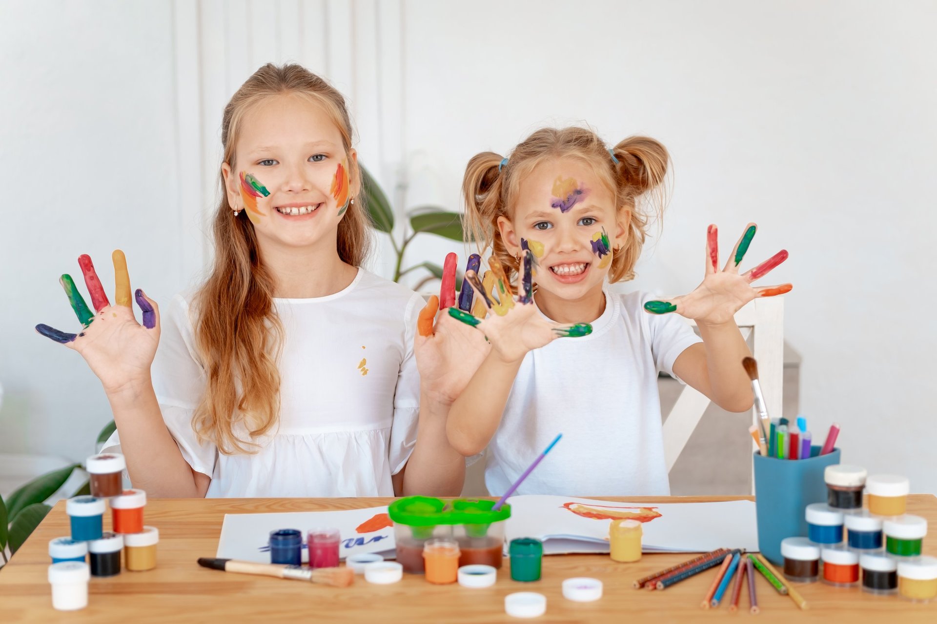 Children drawing with paints, two girls with painted multicolored hands laughing, small artists and children's creativity