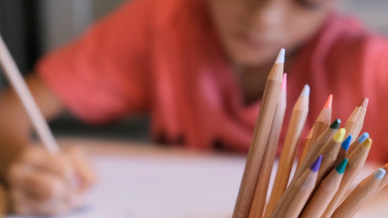 Child drawing with intense focus, colorful pencils in the foreground, capturing childhood creativity and learning