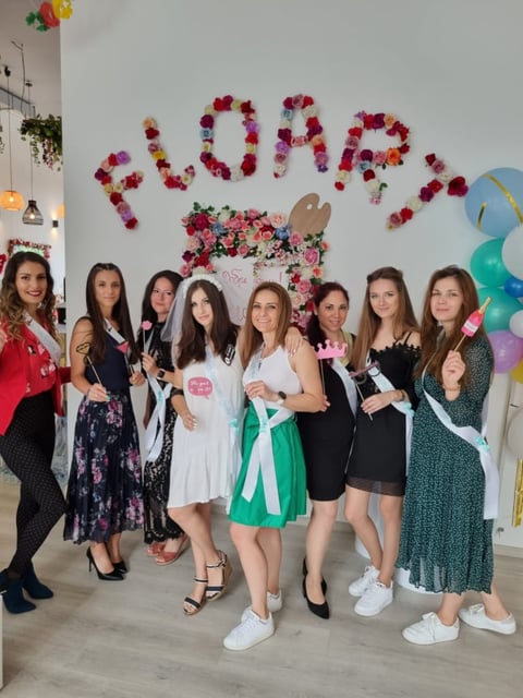 Group of nine women posing together in front of a PROM floral backdrop with colorful balloons at a prom party celebration