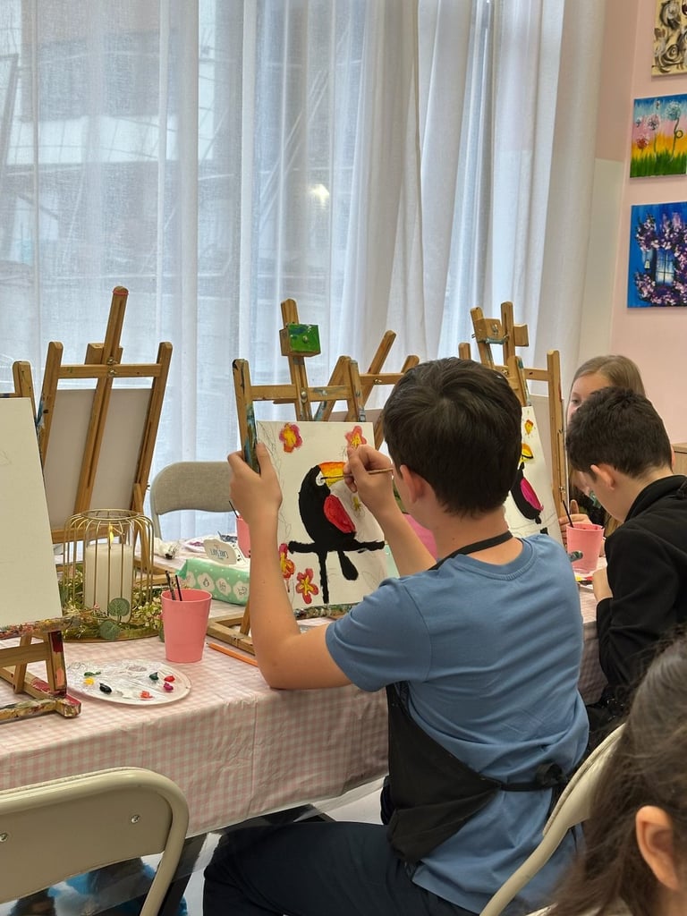Child in blue shirt decorating wooden clothesline with colorful crafts at table with other participants